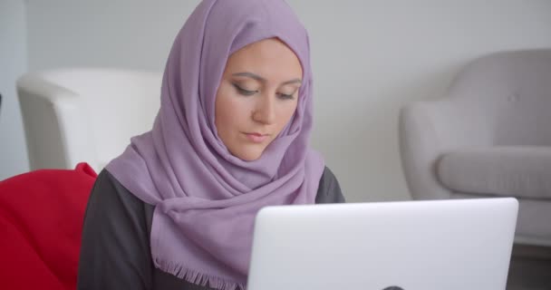 Närbild porträtt av unga muslimska affärskvinna i hijab använder den bärbara datorn sitter i seatbag tittar på kameran leende lyckligt inomhus i lägenheten — Stockvideo