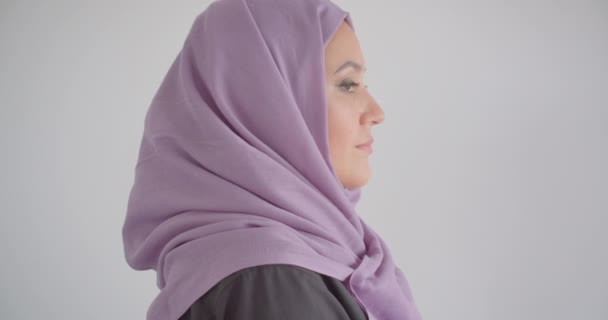 Primo piano vista laterale ritratto di giovane bella donna musulmana in hijab guardando la fotocamera con sfondo isolato in bianco — Video Stock