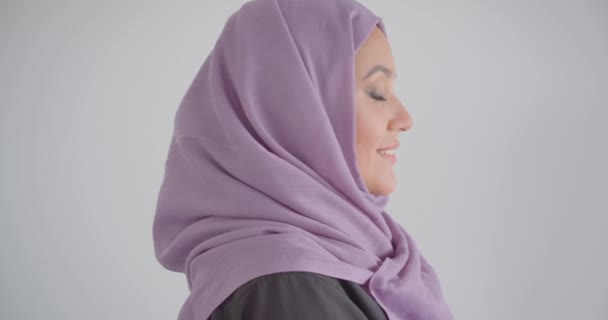 Closeup vista lateral retrato de jovem mulher muçulmana bonita em hijab olhando para a câmera sorrindo alegremente com fundo isolado em branco — Vídeo de Stock