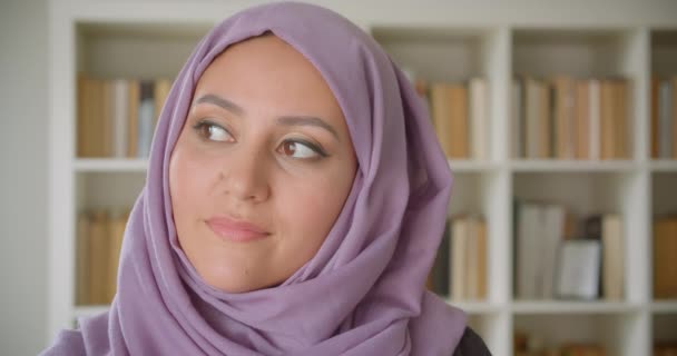 Närbild porträtt av unga ganska muslimska kvinnliga studenten i hijab tittar på kamera leende glatt i biblioteket inomhus — Stockvideo