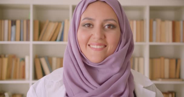 Gros plan portrait de jeune jolie musulmane médecin en hijab regardant la caméra souriant joyeusement dans la bibliothèque — Video