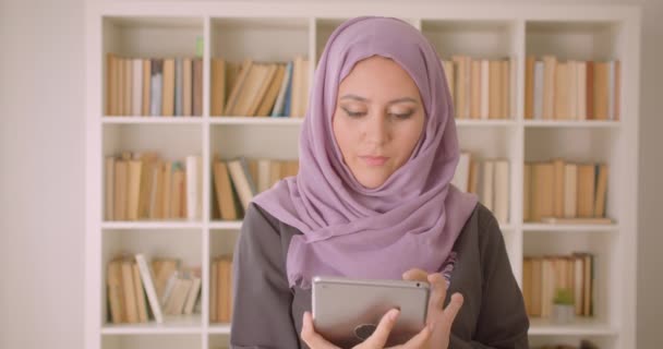 Ritratto ravvicinato di giovane bella donna araba in hijab utilizzando il tablet e mostrando schermo cromatico verde alla fotocamera in biblioteca all'interno — Video Stock