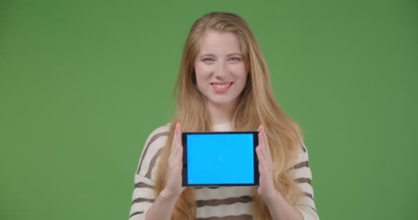Nahaufnahme einer jungen hübschen kaukasischen Frau, die das Tablet benutzt und der Kamera einen blauen Bildschirm zeigt, der glücklich lächelt — Stockvideo