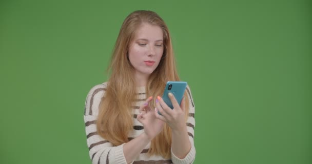 Tembakan jarak dekat dari wanita muda yang cukup Kaukasia menggunakan telepon dan menampilkan layar biru ke kamera — Stok Video