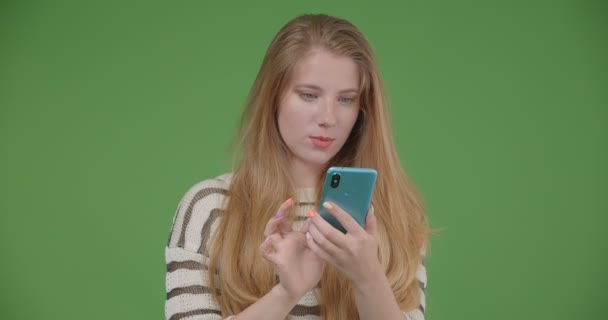 Съемки крупным планом молодой довольно белой женщины с помощью телефона и с голубым экраном на камеру с изолированным на зеленом фоне — стоковое видео