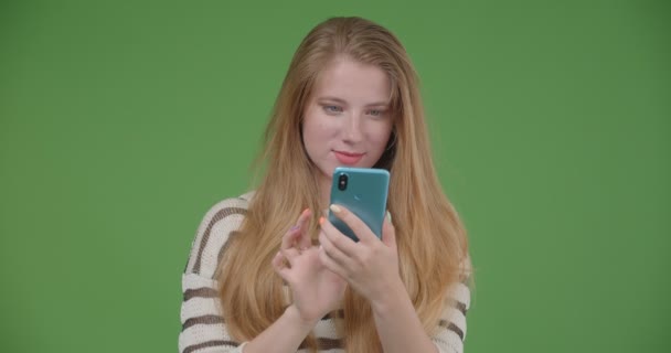 Primer plano de la joven hembra bastante caucásica usando el teléfono y mostrando la pantalla de croma azul a la cámara con fondo aislado en verde — Vídeos de Stock