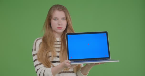 Primer plano de la joven hembra bastante caucásica utilizando el ordenador portátil y mostrando la pantalla azul a la cámara con fondo aislado — Vídeos de Stock