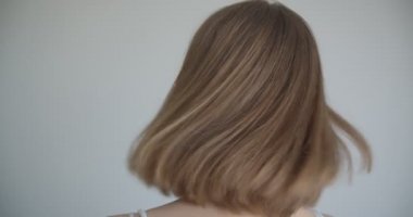 Saç halkaları ve ışıltılı makyaj ile genç güzel beyaz kadın closeup ateş mutlu gülümseyerek ve kapalı beyaz odada kameraya dönerek saçlarını atmak