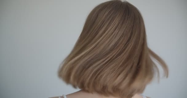 Close-up tiro de jovem muito caucasiano fêmea com anéis de cabelo e maquiagem brilho sorrindo alegremente e jogando seu cabelo se transformando em câmera na sala branca dentro de casa — Vídeo de Stock