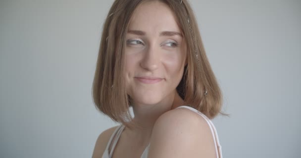 Nahaufnahme einer jungen hübschen kaukasischen Frau mit Haarringen und glitzerndem Make-up, die glücklich zur Seite im weißen Raum drinnen lächelt — Stockvideo