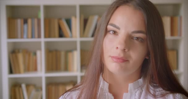 Nahaufnahme Porträt einer jungen hübschen kaukasischen Studentin, die in der Bibliothek fröhlich in die Kamera lächelt — Stockvideo