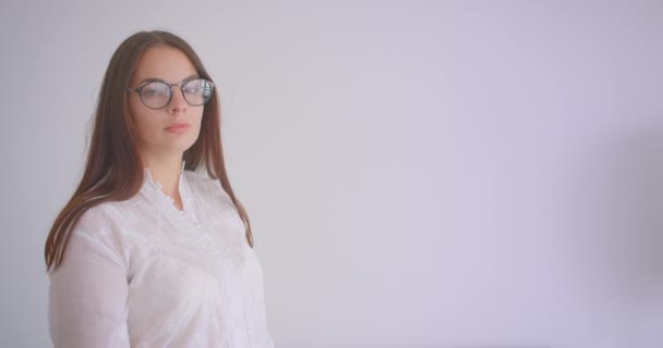 Retrato de cerca de una joven mujer caucásica en gafas mirando a la cámara con los brazos cruzados sobre el pecho con un fondo aislado en blanco — Vídeos de Stock