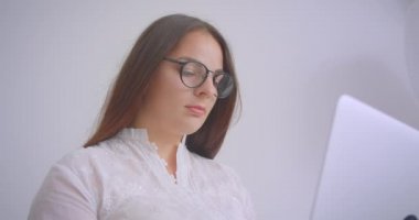Beyaz dairede kapalı kanepede oturan kameraya bakarak dizüstü bilgisayar üzerinde çalışan gözlüklü genç kafkas iş kadının Closeup portre