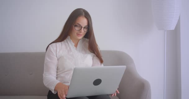 Primer plano retrato de la mujer de negocios caucásica en gafas teniendo una videollamada en el portátil sentado en el sofá interior en el apartamento blanco — Vídeos de Stock