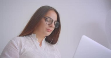 Beyaz ofiste kapalı kanepede oturan kamera bakarak dizüstü bilgisayar üzerinde çalışan gözlük genç başarılı iş kadını Closeup portre