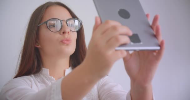 Närbild porträtt av unga kaukasiska affärskvinna i glas tar selfies på tabletten poserar framför kameran sitter på soffan inomhus i vita kontoret — Stockvideo