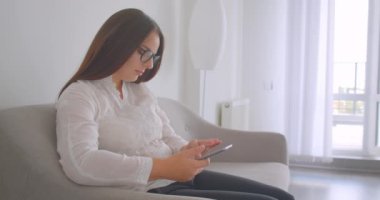 Beyaz dairede kapalı kanepede oturan bir kitap okuma gözlük genç beyaz kadın Closeup yan görünüm portresi