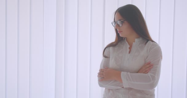 Портрет крупным планом молодой кавказской предпринимательницы в очках, смотрящей в камеру со скрещенными руками над грудью, стоящей в белой квартире — стоковое видео