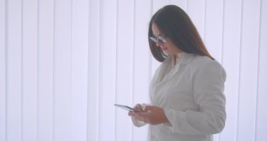 Tableti kullanan ve beyaz dairede kapalı mekanda duran kameraya yeşil ekran gösteren gözlüklü genç beyaz kadın doktorun yakın çekim portresi