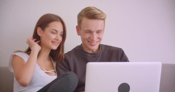 Nahaufnahme Porträt eines jungen netten kaukasischen Paares, das mit dem Laptop einen Film anschaut und zusammen auf der Couch in der Wohnung sitzt — Stockvideo