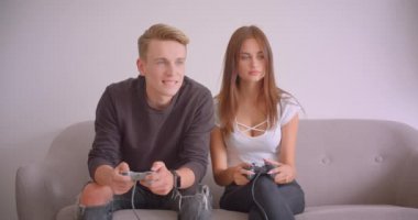 Genç sevimli kafkas çift in closeup portre birlikte daireiçinde kanepede oturan video oyunları oynarken. Kız arkadaşını yenen adam