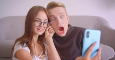 Daire de kapalı telefonda komik selfie'ler çeken genç sevimli kafkas çift closeup portre