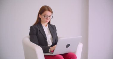 Beyaz dairede koltukta oturan kameraya bakan dizüstü bilgisayar kullanarak gözlükgenç kafkas iş kadının Closeup portre