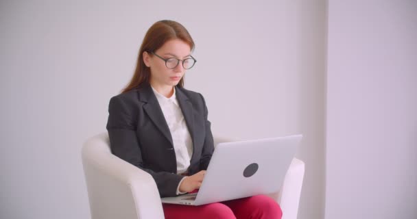 Nahaufnahme Porträt einer jungen kaukasischen Geschäftsfrau mit Brille und Laptop, die im Sessel in der weißen Wohnung sitzt — Stockvideo