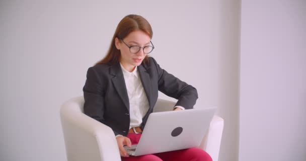 Close-up portret van jonge Kaukasische zakenvrouw in glazen met een video-oproep op de laptop praten vrolijk zittend in de fauteuil in het witte appartement — Stockvideo