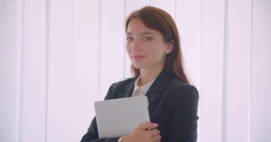 Beyaz ofiste kapalı alanda neşeyle gülümseyen kameraya bakan dizüstü bilgisayarı tutan genç beyaz iş kadınının yakın çekim portresi