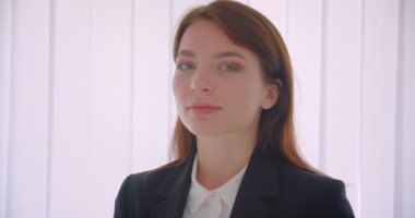 Beyaz ofiste evde mutlu bir şekilde ayakta duran kameraya bakan genç başarılı iş kadınının yakın çekim portresi