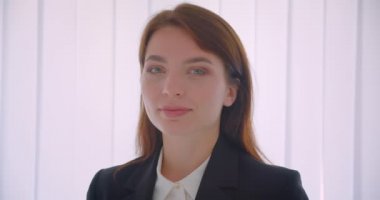 Beyaz ofiste içeride neşeyle ayakta duran kameraya bakan genç başarılı iş kadınının yakın çekim portresi