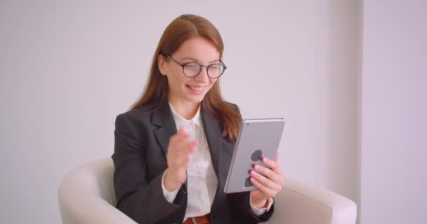 Closeup portré fiatal kaukázusi üzletasszony a szemüveg, amelynek videohívás a tabletta integetett Szia ül a karosszékben a fehér lakásban — Stock videók