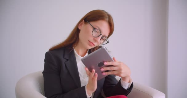 Closeup retrato de jovem empresária alegre em óculos digitando no tablet olhando ta câmera sorrindo feliz sentado na poltrona — Vídeo de Stock