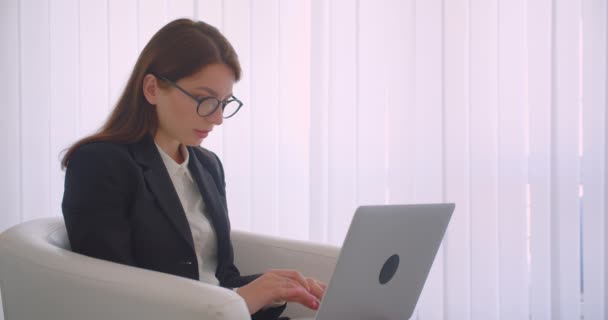 Primer plano vista lateral retrato de joven mujer de negocios caucásica en gafas de trabajo en el portátil mirando a la cámara sonriendo felizmente sentado en el sillón — Vídeos de Stock