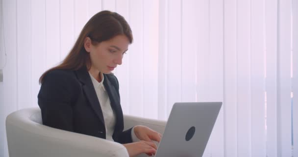 Close-up vista lateral retrato de jovem mulher de negócios caucasiana usando o laptop olhando para a câmera sorrindo feliz sentado na poltrona — Vídeo de Stock