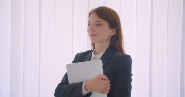 Zbliżenie Portret młodej kaukaski biznesmen trzymając laptopa patrząc na kamerę stojącą wewnątrz w białym biurze — Wideo stockowe
