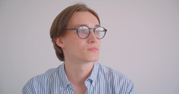 Крупним планом портрет молодого привабливого кавказького бізнесмена в окулярах дивиться на камеру, усміхаючись весело в приміщенні в білій квартирі — стокове відео