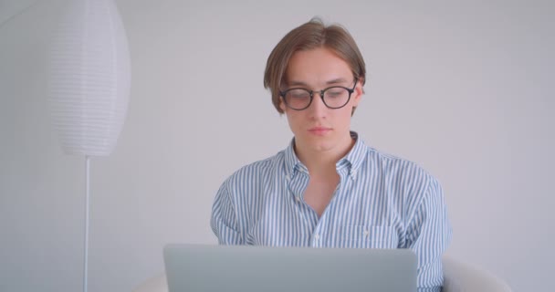 Gros plan portrait de jeune homme d'affaires caucasien attrayant travaillant sur l'ordinateur portable regardant la caméra souriant joyeusement assis dans le fauteuil à l'intérieur — Video