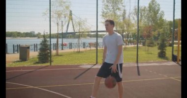 Genç beyaz erkek basketbolcu arka planda köprü ile açık sahada pota bir top atma Closeup portre
