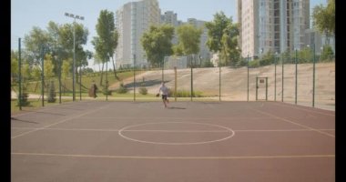 Genç beyaz erkek basketbolcu arka planda şehir binaları ile sahada pota bir top atma closeup portre