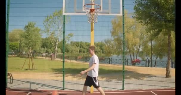 코트에서 농구공을 던지는 젊은 매력적인 백인 남성 농구 선수의 클로즈업 초상화가 공원을 이겼습니다. — 비디오