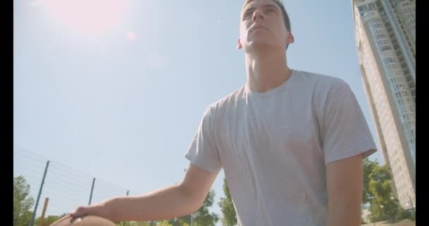 Closeup retrato de jovem atlético caucasiano jogador de basquete masculino jogando uma bola no aro na quadra no parque — Vídeo de Stock