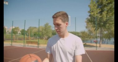 Genç çekici beyaz erkek basketbolcu arka planda köprü ile açık sahada çember bir top atma Closeup portre