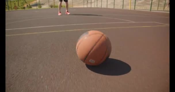 Retrato de primer plano del joven jugador de baloncesto caucásico activo lanzando pelota en el aro en la cancha con edificios en el fondo — Vídeo de stock