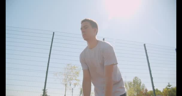 Closeup retrato de jovem caucasiano jogador de basquete masculino jogando uma bola em aro na quadra ao ar livre com ponte no fundo — Vídeo de Stock