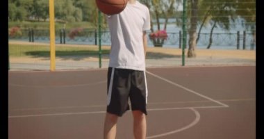 Genç yakışıklı beyaz erkek basketbolcu arka planda köprü ile açık havada kamera bakarak bir top tutan closeup portre