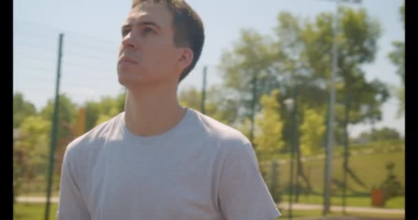 Closeup portrét fotoaparátem, který se pohybuje kolem pohledného bělošského basketbalového hráče, který hází míč na dvůr venku v městském městě — Stock video