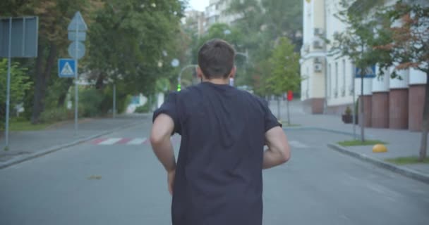 Closeup back view portrait of adult caucasian sporty male jogger walking down the street in the urban city outdoors — Stock Video