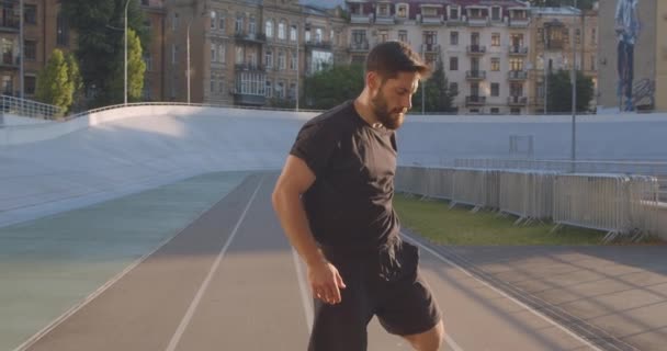 Primo piano ritratto di adulto caucasico sportivo corridore maschile riscaldamento e jogging sullo stadio nella città urbana all'aperto — Video Stock